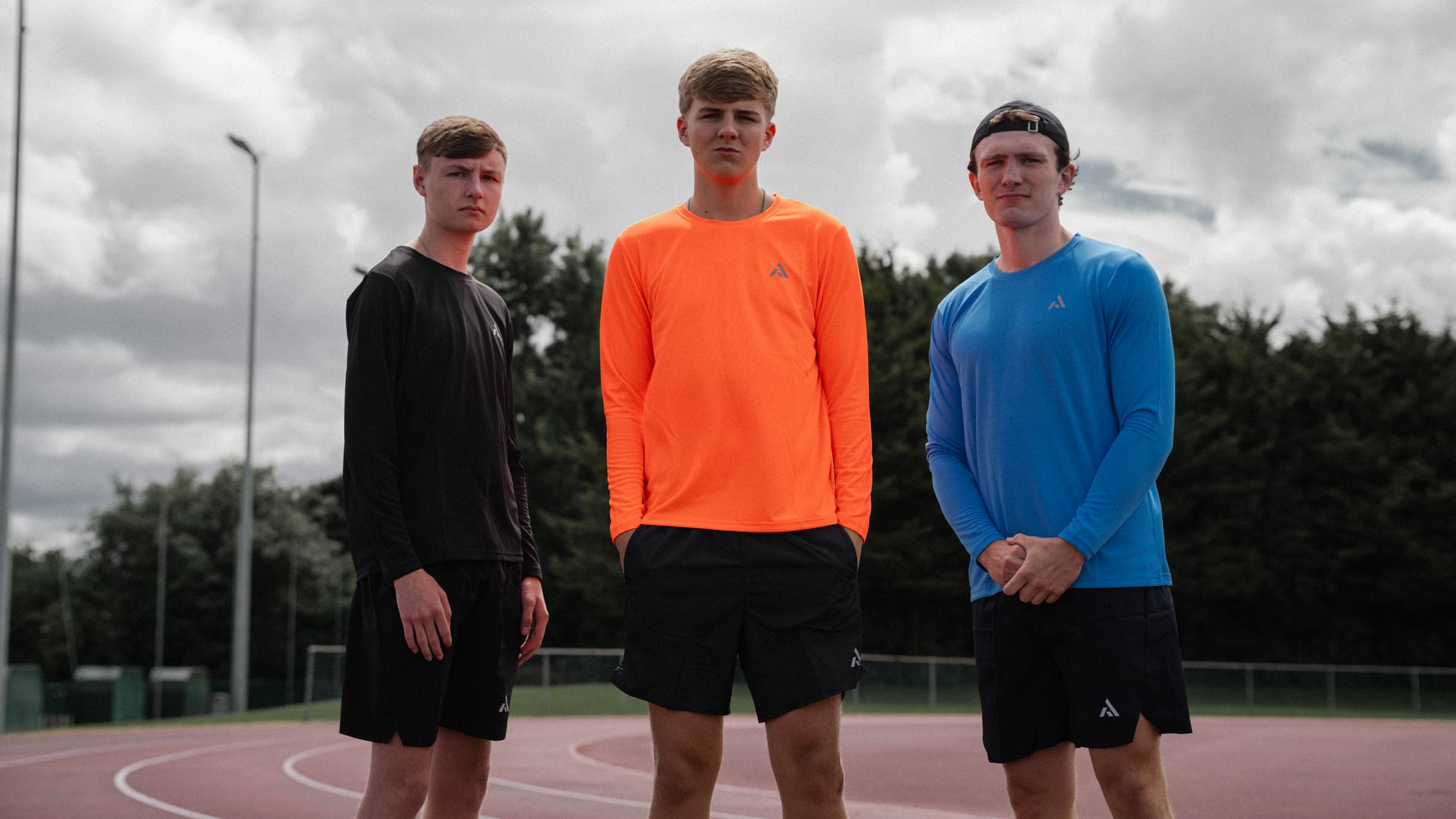 Three athletes on the track in PEAK long-sleeves and shorts, under a heavy grey sky